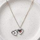 Silver birthstone heart locket necklace open on a speckled ceramic plate
