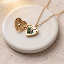 Gold birthstone heart locket necklace open on a glossy ceramic plate, showing the photo inside
