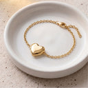 Gold heart locket bracelet resting on a speckled ceramic plate
