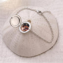 Silver photo locket bracelet open to show a personalised photo inside, draped over a textured ceramic dome
