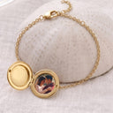 Gold photo locket bracelet open to reveal a custom photo inside, resting on a textured ceramic dome
