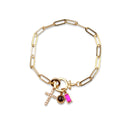 A gold paperclip chain bracelet with three charms: a gold cross, a round dark brown stone, and a rectangular pink gemstone, displayed on a clean white background.