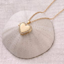 Gold Sparkling Heart Locket Necklace resting on a textured ceramic dome, heart locket closed

