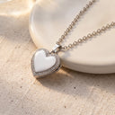 Gold Sparkling Heart Locket Necklace with zirconia border closed, displayed beside ceramic plates

