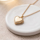 Gold heart locket necklace with polished heart closed, on a white background
