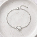 Silver heart locket bracelet with polished heart closed, resting on a speckled ceramic plate
