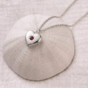 Silver birthstone heart locket necklace open on a textured ceramic dome, revealing the custom photo inside
