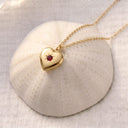 Gold birthstone heart locket necklace closed, resting on a textured ceramic dome
