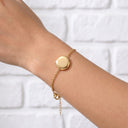 Gold Always With You Locket Bracelet worn on a wrist against a white brick wall
