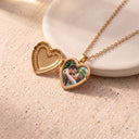 Gold heart photo locket necklace open to show a personalised photo, resting on a textured ceramic dome
